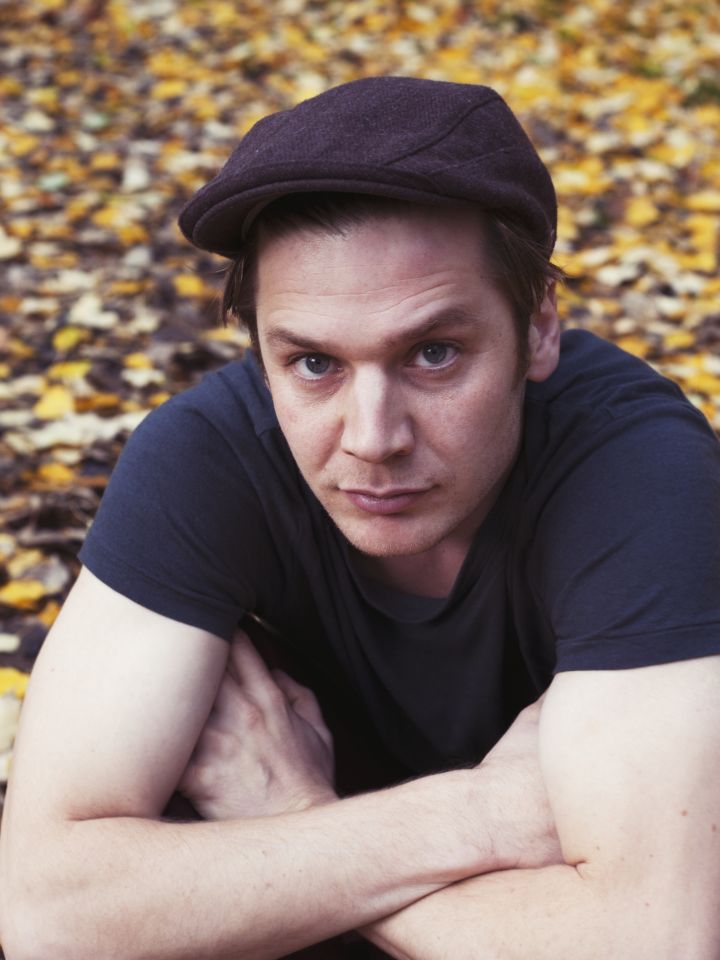 Das Foto zeigt ein Porträt von Justin Mühlenhardt zwischen Herbstblättern. Er trägt eine Kappe.